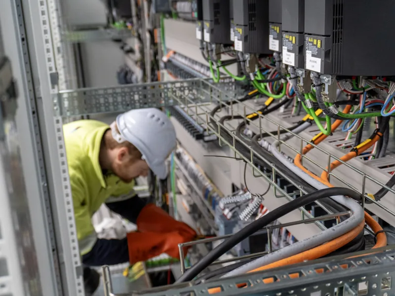 Electrician working on control panel wiring and cable tray in a plant room